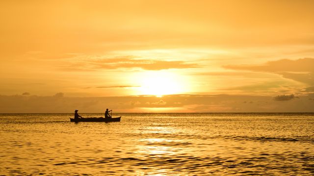 Fishermen silhouetted against a breathtaking golden sunset, peaceful sea stretches out to the horizon. Ideal for nature-inspired designs, relaxation themes, travel brochures, and evening scene settings.