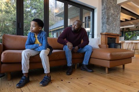 African american father and son sharing tense moment on leather sofa in modern living room