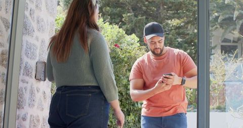 Couple standing at front door checking smartphone and door keypad on sunny day