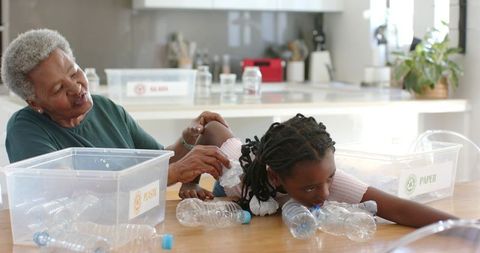 African American grandmother teaching child to sort plastic and paper for recycling