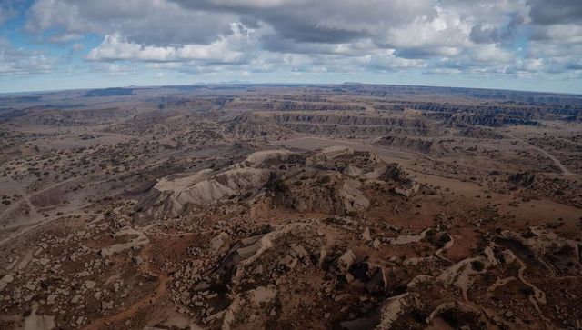 Aerial view revealing terraced erosion and layered badlands plateau under dramatic clouds