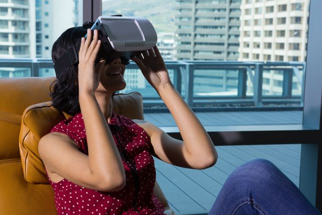 Woman experiencing virtual reality with a VR headset, sitting comfortably in a modern office environment with large windows. Ideal for showcasing innovation, technology in office spaces, virtual reality trends, and the modern workplace.