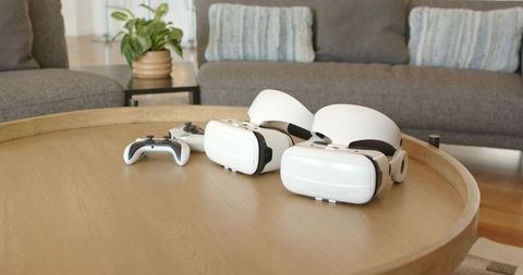 Two vr headsets and wireless controller resting on wooden coffee table in modern lounge