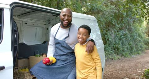 Smiling african american vendor and son selling fresh produce from mobile market van