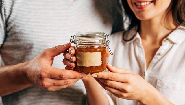 Couple holding homemade jam in clamp-lid glass jar with kraft label, sharing gift