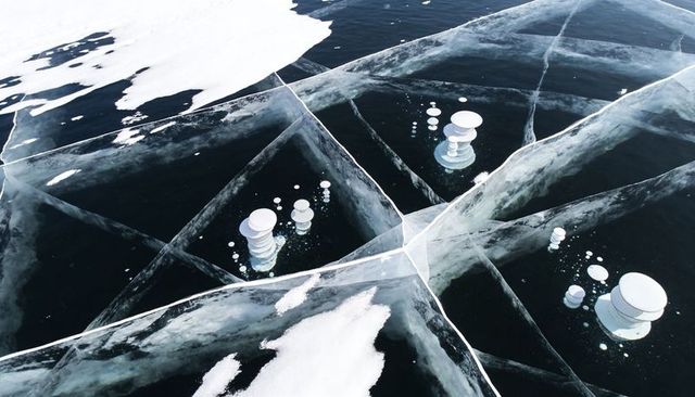 Aerial topdown of clear lake ice with intersecting pale cracks and stacked methane bubbles