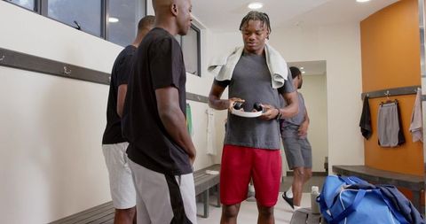 Athletes preparing in locker room holding headphones and towel, team bonding