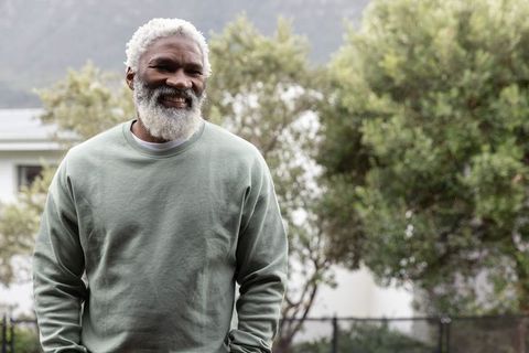 Smiling senior african american man standing outdoors in sage sweatshirt, relaxing at home