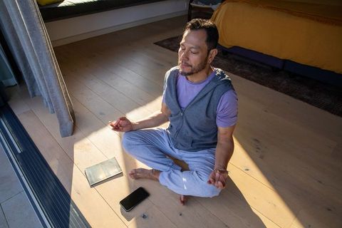 Asian man meditating in morning sun near glass door mindfulness practice in minimal bedroom