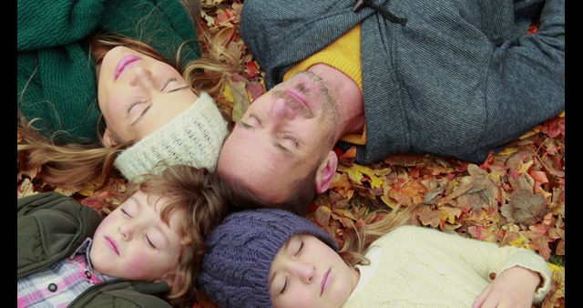 Family enjoying a peaceful moment lying on colorful autumn leaves. Idea for use in seasonal promotional materials, lifestyle blogs, and imagery focusing on family bonding, nature, and relaxation during the fall season.