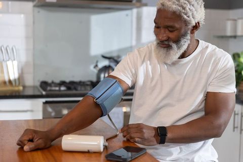 Senior african american man checking blood pressure at home using smartwatch and cuff