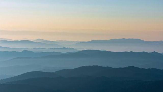 Mist-draped mountain ridges welcoming dawn with layered horizons and pastel sky