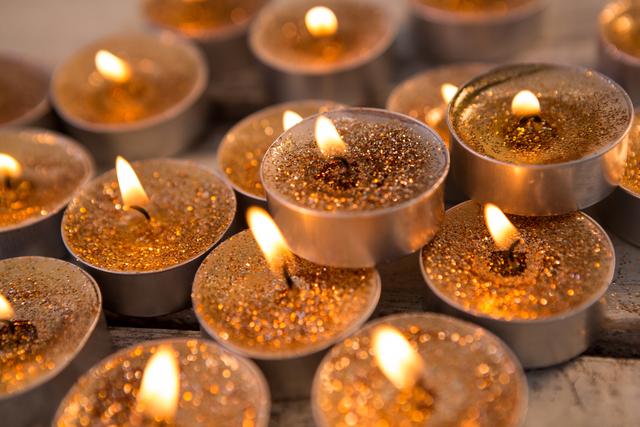 Tea light candles with golden glitter burning on a wooden plank, creating a warm and festive ambiance. Ideal for use in holiday-themed projects, Christmas decorations, relaxation and spa settings, or any celebration needing a cozy and inviting atmosphere.