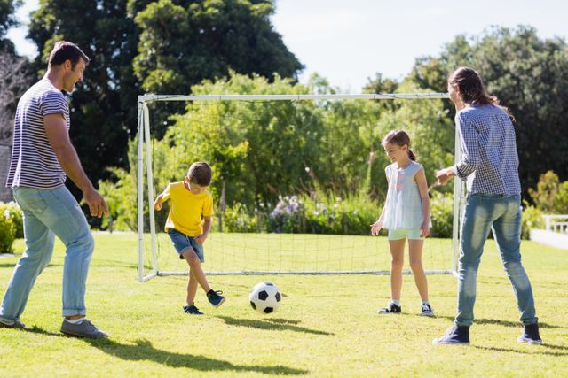 Family enjoying a sunny day playing football in a park. Parents and children bonding through outdoor activities. Ideal for promoting family time, outdoor recreation, and healthy living.
