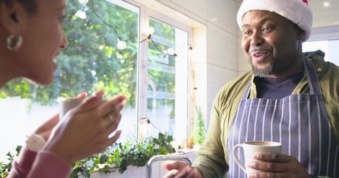 Couple sharing hot drinks in cozy kitchen with African American man wearing Santa hat