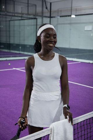 African american tennis player smiling on purple indoor court wearing white athletic outfit
