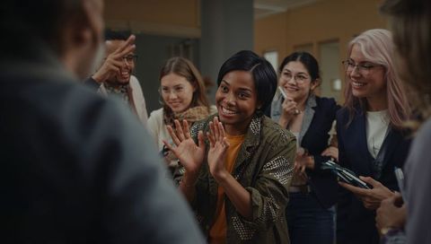 Applauding team celebrating colleague success in office corridor with smiling colleagues