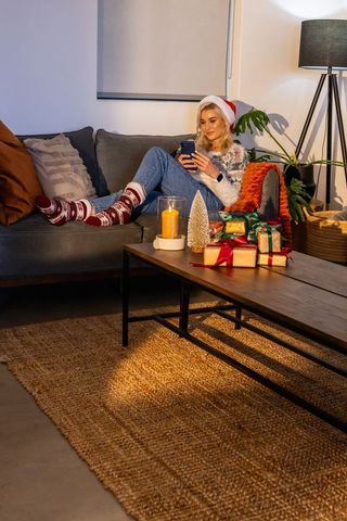 Young woman relaxing on sofa during cozy christmas evening using smartphone
