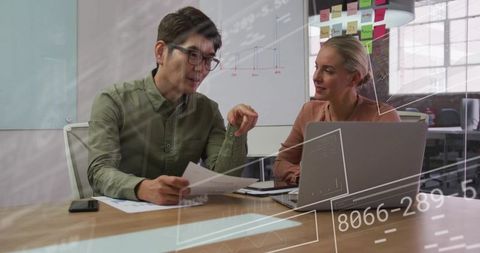 Collaborating on data analytics and strategy with laptop and reports in open-plan office