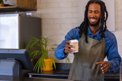 Smiling african american barista handing takeaway coffee cup over counter in modern cafe