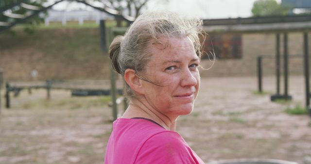 Portrait of happy mature caucasian woman in pink t shirt turning and smiling at bootcamp. Female fitness, challenge and healthy lifestyle.