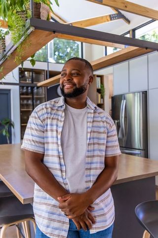 Smiling black man standing in bright modern kitchen with hanging plant shelf
