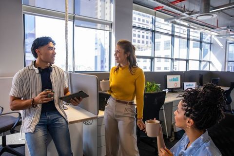 Casual coworkers chatting and collaborating during coffee break in modern open-plan office