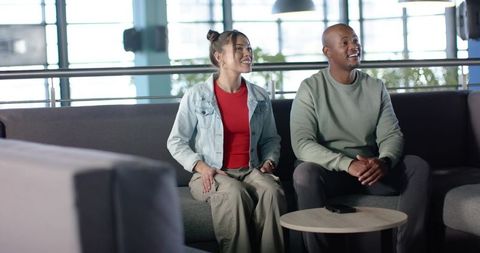 Multicultural young couple sitting in modern office lounge smiling and holding smartphone