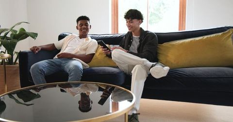 Young Diverse Friends Sharing Phone on Modern Velvet Sofa in Sunlit Living Room