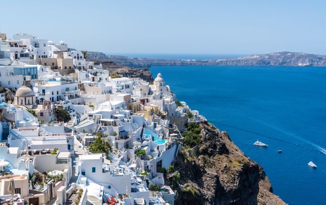 This image captures a stunning cliffside village in Santorini, Greece, overlooking the deep blue Aegean Sea. The iconic white buildings with blue rooftops present a picturesque view that is synonymous with Mediterranean architecture. Ideal for travel blogs, tourism brochures, or holiday destination advertising, showcasing one of Europe’s most romantic and scenic locations.