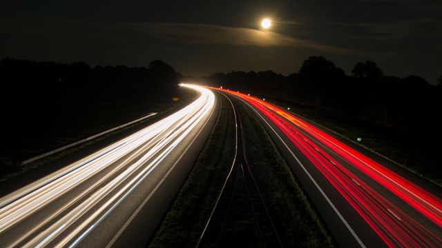 Capturing light trails from vehicles on a highway at night under a full moon, this image highlights motion, speed, and the dynamic nature of transportation. Perfect for use in advertisements, technology websites, and travel blogs, conveying themes of movement, travel, and nighttime activity. It can also be used to illustrate concepts related to traffic flow and road safety.