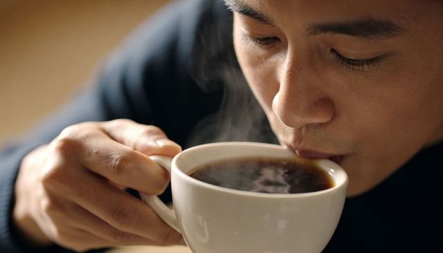 Sipping black coffee by asian man in cozy cafe closeup steam rising warm morning moment