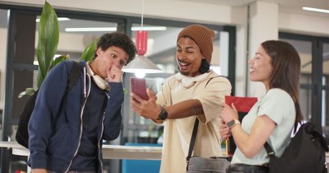 African american student showing smartphone to college friends in modern campus lounge