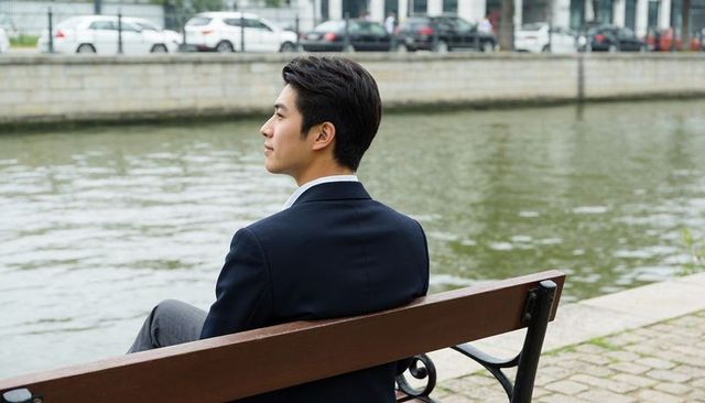 Businessman in navy suit sitting on riverside bench gazing at urban canal for quiet reflection