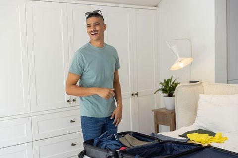 Young man packing suitcase on bed preparing for weekend trip in bright minimalist bedroom