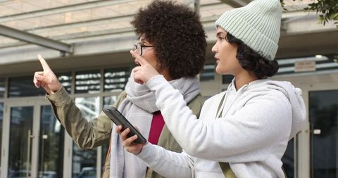 Young women navigating urban entrance using smartphone while pointing toward building