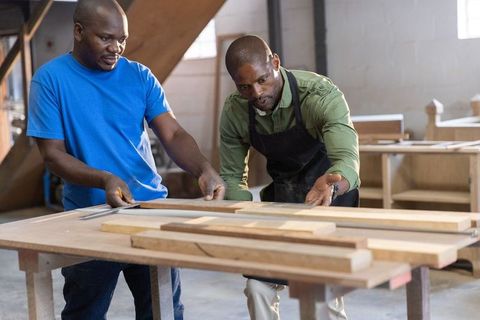 African american woodworkers measuring and aligning wooden planks in carpentry workshop