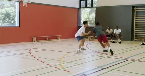 African american teen dribbling and shooting jumpers while defender closing in indoor court