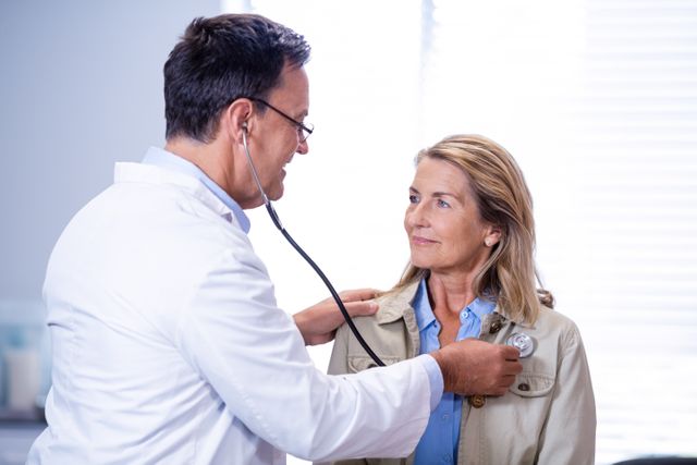 Doctor examining female patient with stethoscope in hospital. Ideal for healthcare, medical consultation, patient care, and health-related content. Useful for illustrating doctor-patient interactions, medical check-ups, and professional healthcare services.