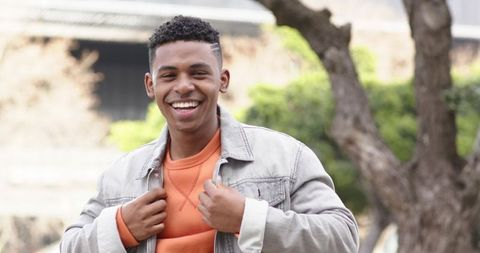 Confident African American Man Smiling Outdoors Adjusting Denim Jacket and Orange Sweatshirt