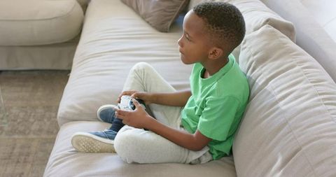 African american boy playing video games on beige couch at home