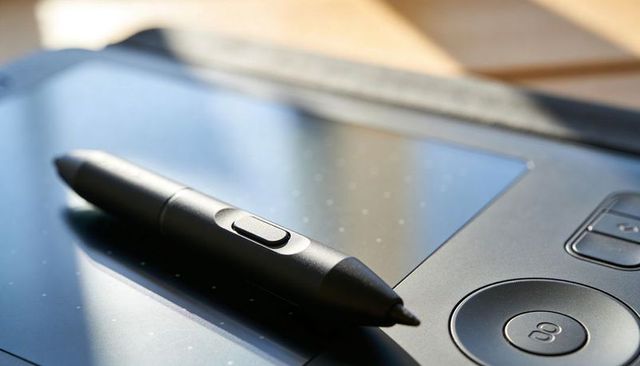 Black stylus pen resting on digital drawing tablet with control dial and natural light