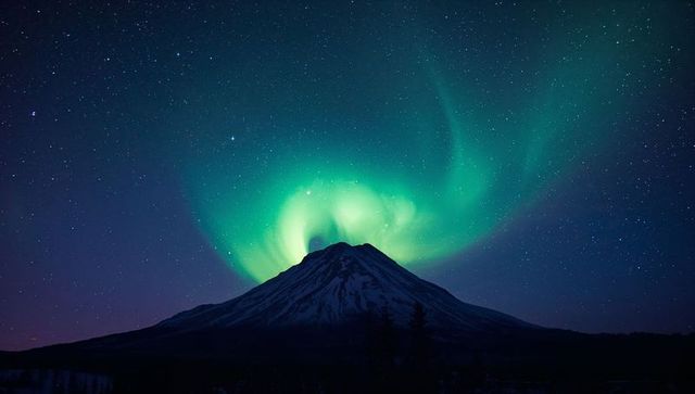 Green aurora crowning snow-capped mountain peak like glowing halo under starry night sky