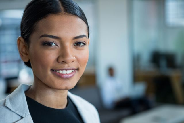 Businesswoman smiling confidently in a modern office environment. Ideal for use in corporate websites, business presentations, career-related articles, and professional networking profiles.