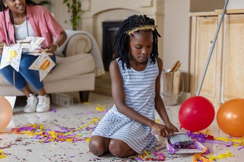 African american mother and daughter cleaning up confetti and balloons after party