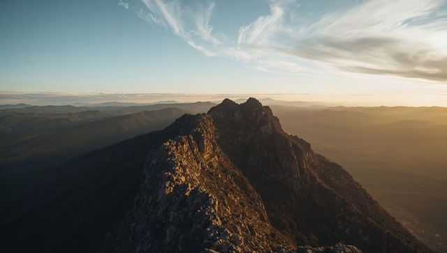 Jagged rocky ridge glowing in golden sunset light across misty alpine panorama