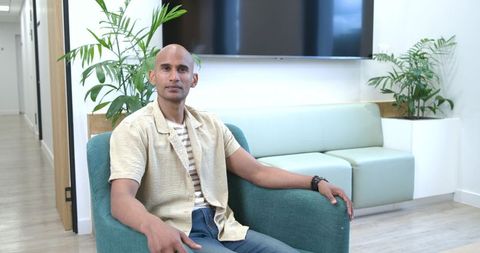 African american man sitting in modern reception area with teal chair and casual outfit