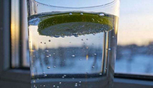 Close-up sparkling water with floating lime slice on window sill at golden hour