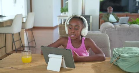African american girl learning on tablet with headphones in modern open-plan home