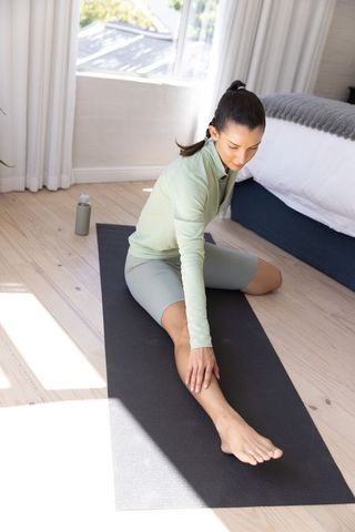 Sunlit bedroom hamstring stretch on yoga mat for home fitness and mindful wellness